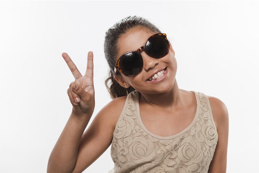 Imagen de una niña con gafas realizando el símbolo de la V con los dedos