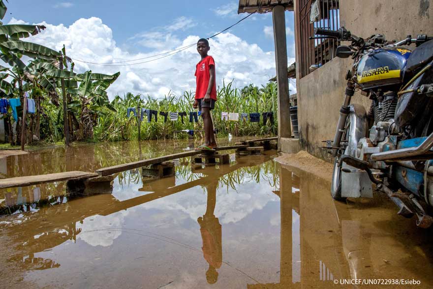 Un niño de pie sobre una pasarela de madera improvisada frente a su casa afectada por la las inundaciones