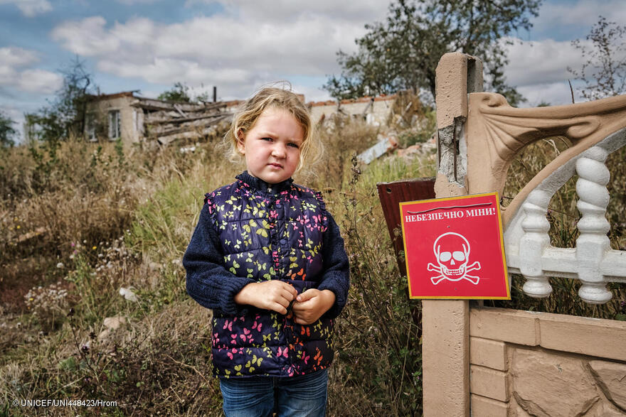Una niña ucraniana junto a una señal que advierte del peligro de minas