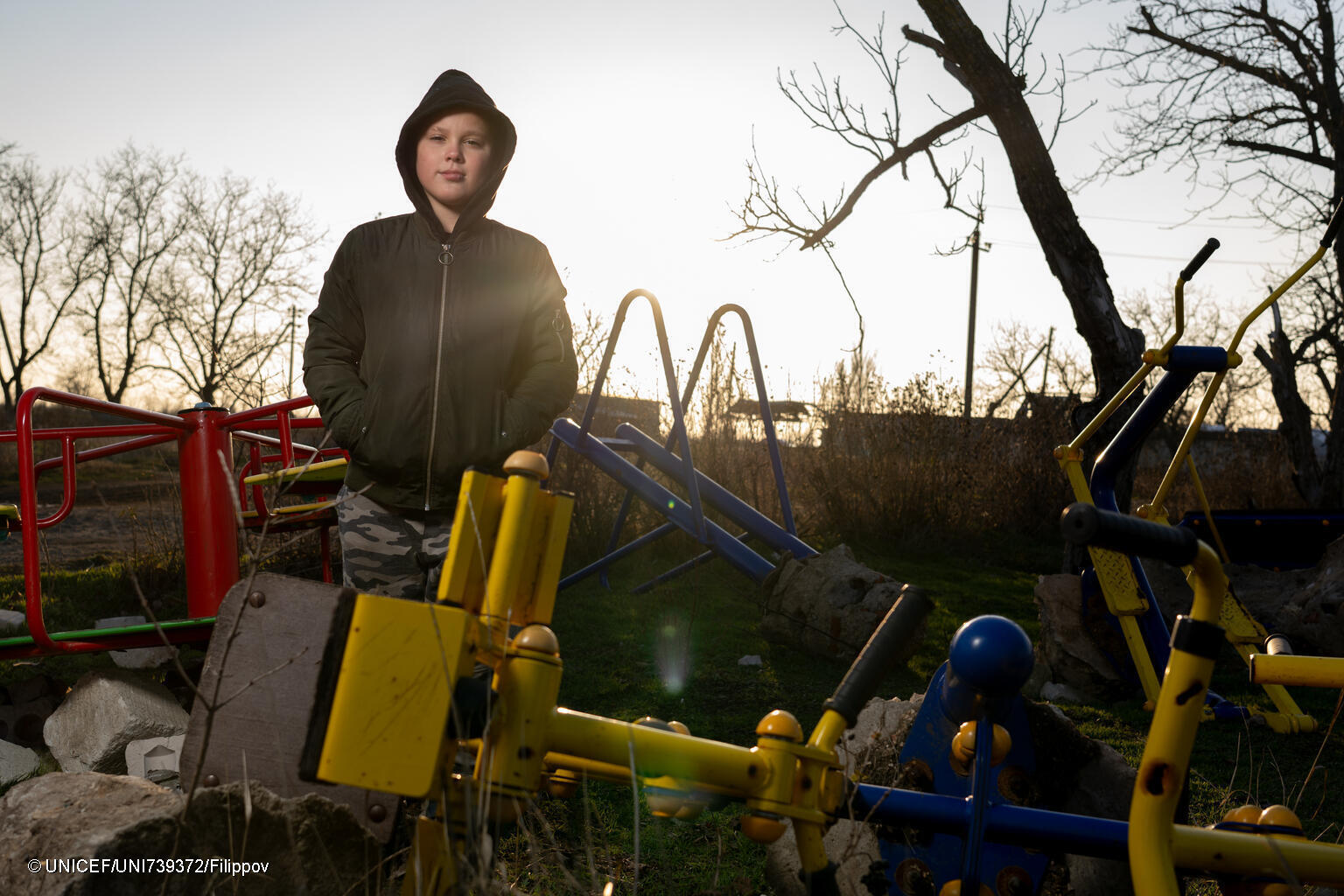 Niño a contraluz del sol, rodeado de columpios rotos