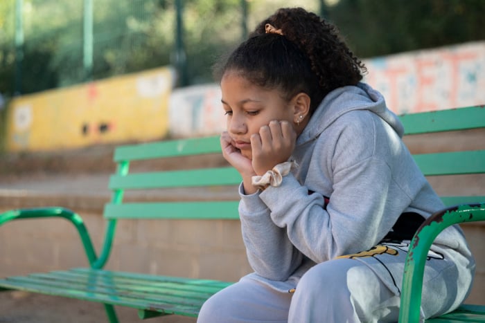 Una niña sentada en un banco pensando.