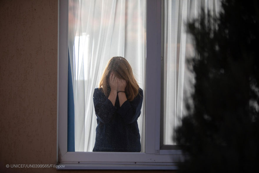 Una niña se tapa la cara tras una ventana. Imagen de recurso