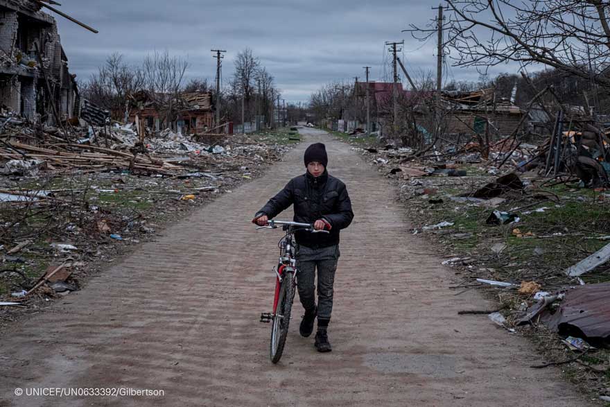 Un niño camina con su bicicleta junto a casas destruidas cerca de la suya en Ucrania