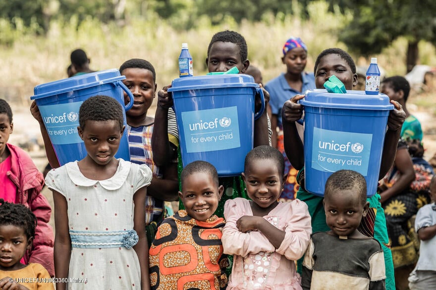 Niños y niñas sostienen cubos de agua limpia suministrados por UNICEF en Malawi