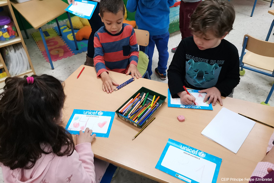 Dos niños y una niña decoran sus dorsales en un aula