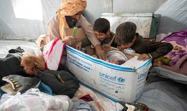 Una familia abre una caja de suministros dentro de una tienda de campaña de UNICEF