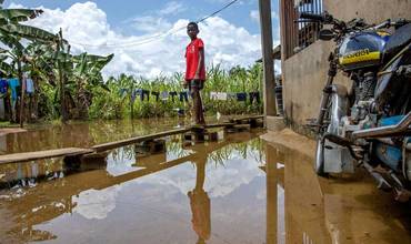 Un niño de pie sobre una pasarela de madera improvisada frente a su casa afectada por la las inundaciones