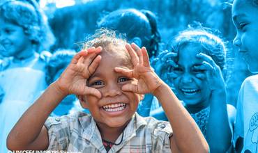 Niña sonriente jugando con sus manos como si llevara unas gafas imaginarias.