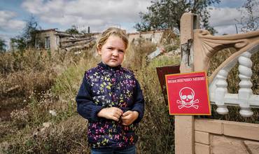 Una niña ucraniana junto a una señal que advierte del peligro de minas