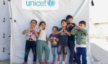 Un grupo de niños frente a un aula en una tienda de campaña apoyada por UNICEF en un campamento informal de Hatay, Turquía