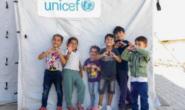 Un grupo de niños frente a un aula en una tienda de campaña apoyada por UNICEF en un campamento informal de Hatay, Turquía