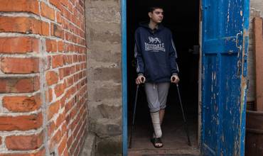 Yaroslav, de 16 años, que perdió la pierna derecha por la explosión de una mina hace seis meses y ya no puede andar. El chico está de pie con sus muletas junto a su casa. (Ucrania)