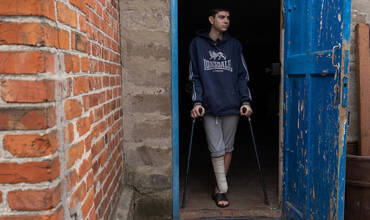Yaroslav, de 16 años, que perdió la pierna derecha por la explosión de una mina hace seis meses y ya no puede andar. El chico está de pie con sus muletas junto a su casa. (Ucrania)