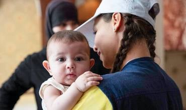Una trabajadora nutricional de un equipo móvil apoyado por UNICEF sostiene a Samar, de 5 meses, y la prepara para un control de peso
