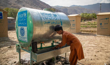 niño afgano bebiendo de uno de los suministros de agua instalados por UNICEF en un campo de refugiados