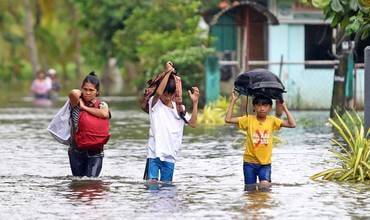 niños y niñascon el agua a la altura de sus rodillas desplazándose con sus mochilas en alto