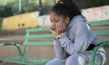 Una niña sentada en un banco pensando.