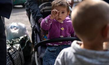 Faina, un bebé de un año, está sentada en un cochecito en la parada de autobús del pueblo de Dachne, en Ucrania, esperando un autobús para evacuar la zona y huir de los bombardeos..