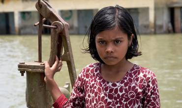 Una niña de Bangladesh delante de la única fuente de agua limpia de su entorno escolar.