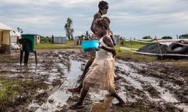 Una niña camina por un terreno embarrado con un barreño en las manos
