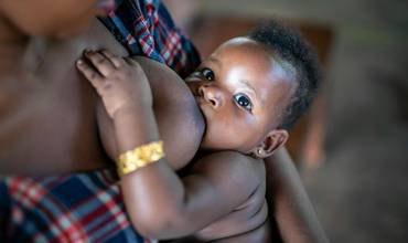 El 13 de marzo de 2024 en Jinja, Uganda, una madre amamanta a su bebé mientras esperan su turno para la vacunación en la clínica para niños pequeños del hospital de referencia de Jinja.