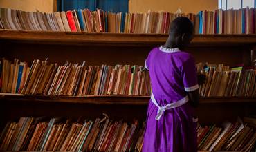 Una niña busca un libro que leer en la biblioteca de su escuela en Uganda