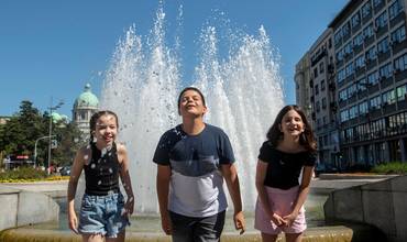 Tres niños combaten el calor en una fuente en una ciudad europea