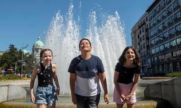 Tres niños combaten el calor en una fuente en una ciudad europea
