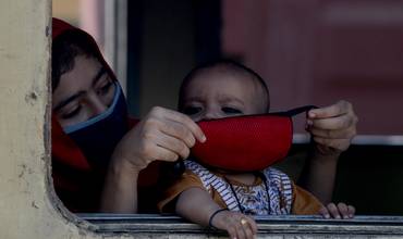 Una madre le coloca la mascarilla a su bebé en un tren en India