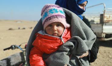 Una niña pequeña sonríe mientras su madre espera recibir el kit de invierno de su familia, distribuido por UNICEF