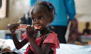 Una niña toma un sobre de alimento terapéutico en Sudán