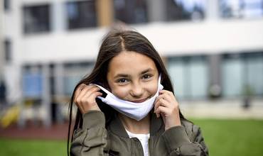 Una niña sonríe mientras se pone una mascarilla