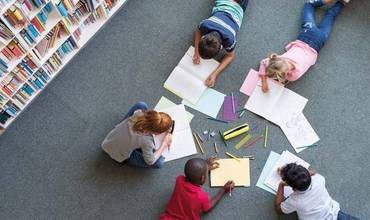 Un grupo de niños y niñas dibujan en el el suelo de una biblioteca