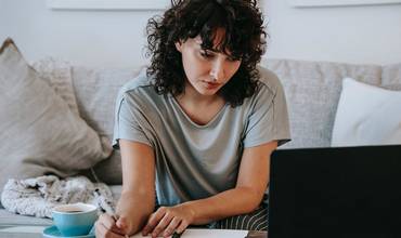 Una mujer toma notas frente a un portátil