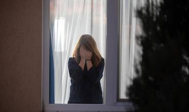 Una niña se tapa la cara tras una ventana. Imagen de recurso