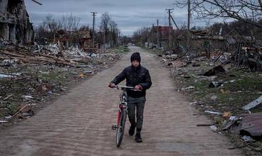 Un niño camina con su bicicleta junto a casas destruidas cerca de la suya en Ucrania