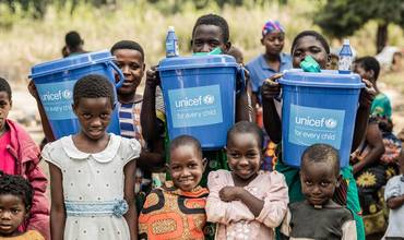 Niños y niñas sostienen cubos de agua limpia suministrados por UNICEF en Malawi