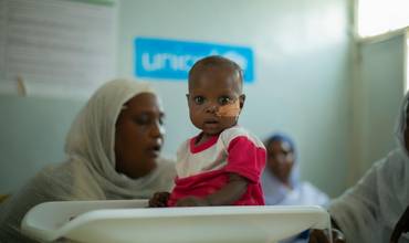 Un bebé sudanés sentado sobre una báscula en una de las clínicas que UNICEF apoya en el país