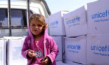 Una niña siria junto a los suministros de UNICEF distribuidos en su campamento de desplazados