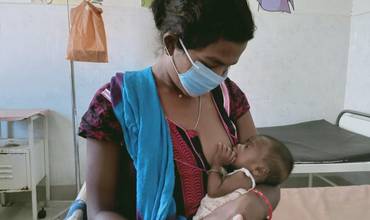 Una mujer con mascarilla da el pecho a su bebé en India