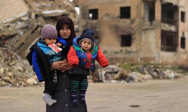 Una madre sostiene en brazos a sus dos hijos en Siria.