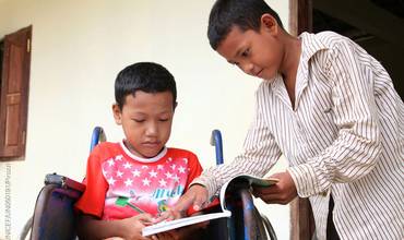 Un niño con discapacidad comparte un libro con un amigo en su escuela de Camboya.