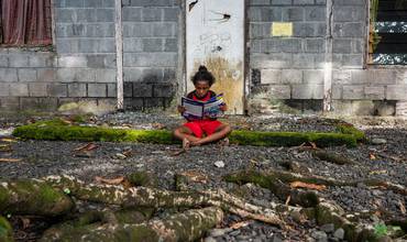 Una niña lee a las puertas de su casa en Indonesia