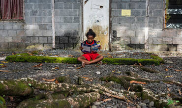 Una niña lee a las puertas de su casa en Indonesia
