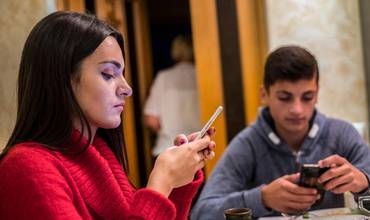 Dos adolescentes utilizan su teléfono móvil durante la comida