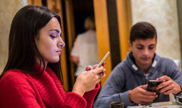 Dos adolescentes utilizan su teléfono móvil durante la comida
