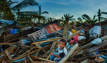 Un niño se sienta entre los escombros de las casas destrozadas por el tifón