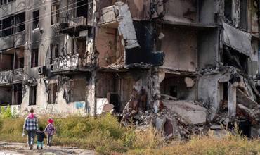 Una madre y dos niños ucranianos caminando al lado de un edificio en ruinas