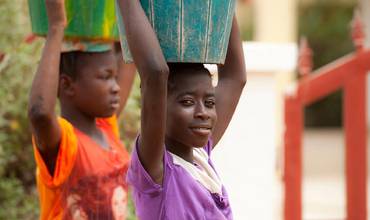 Niñas transportando cubos de agua sobre la cabeza