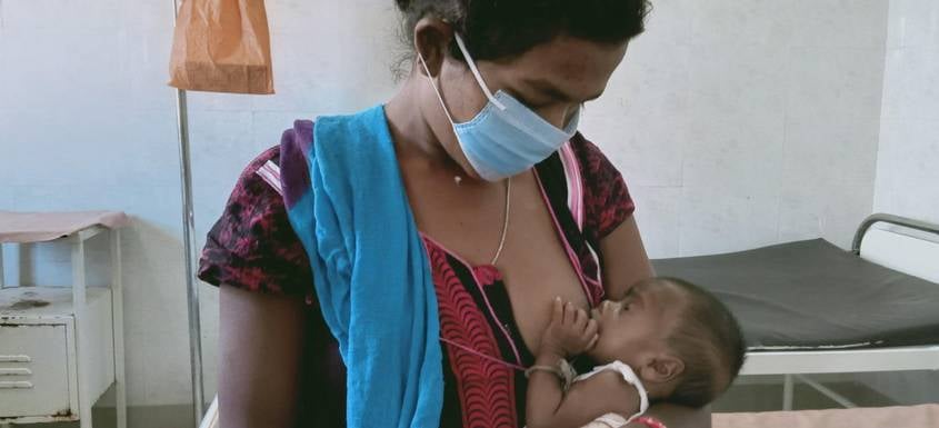 Una mujer con mascarilla da el pecho a su bebé en India